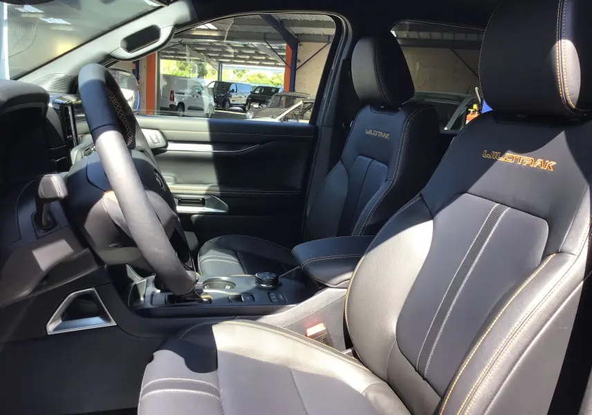 Vue intérieure côté conducteur du Ford Ranger Wildtrak 2025 avec sièges cuir noirs et surpiqûres orange visibles.