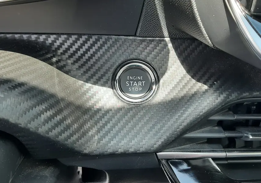 Bouton start/stop moteur sur tableau de bord avec finition carbone à l'intérieur d'un Peugeot 2008 gris Artense 2022.