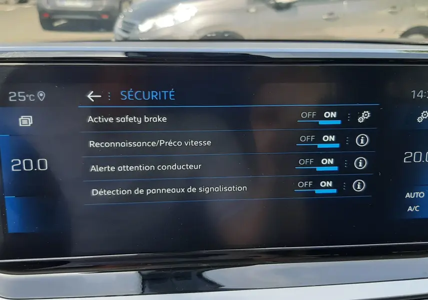 Écran central du Peugeot 2008 2022 montrant les réglages de sécurité avec vue floue sur parking extérieur en arrière-plan.