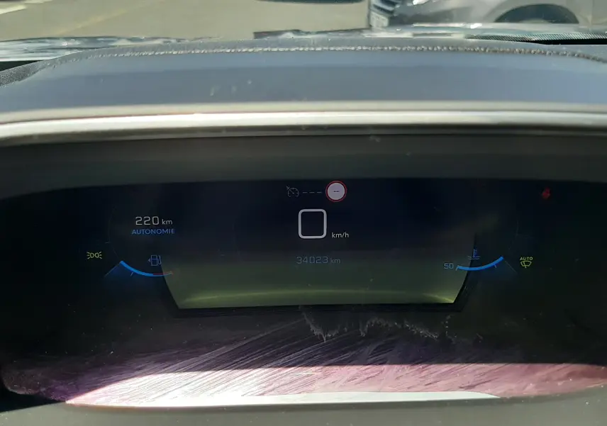 Tableau de bord numérique du Peugeot 2008 gris Artense, affichant 220 km d'autonomie et 34 023 km au compteur, vue de face.