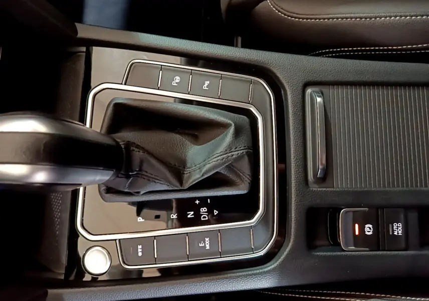 Gros plan sur la console centrale noire de la Volkswagen Passat hybride rechargeable, avec levier de vitesse automatique et boutons de contrôle.