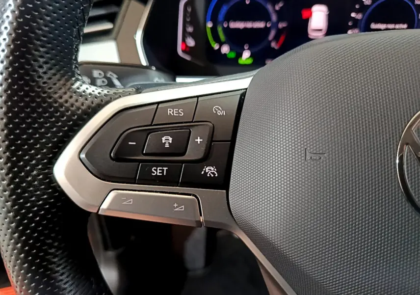 Gros plan sur les commandes du volant à gauche de la Volkswagen Passat hybride rechargeable 2022, avec tableau de bord numérique.