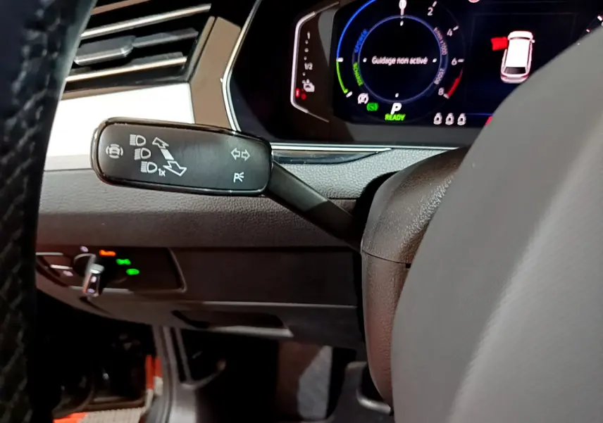 Gros plan sur la manette de clignotants à gauche du volant d'une Volkswagen Passat hybride rechargeable, tableau de bord numérique visible.