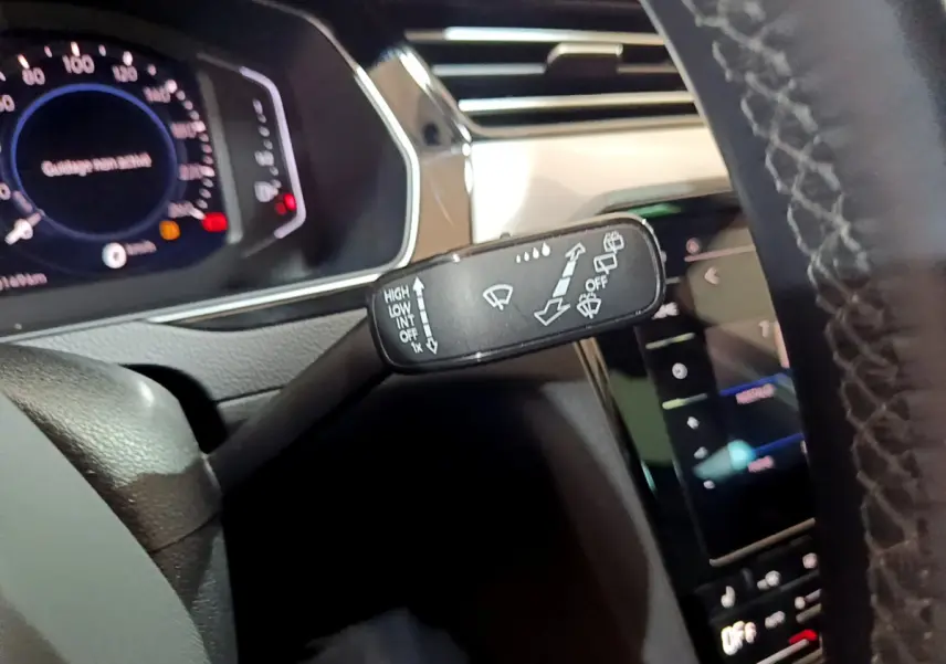 Gros plan sur la commande d’essuie-glace à gauche du volant dans l’habitacle gris foncé de la Volkswagen Passat hybride rechargeable 2022.