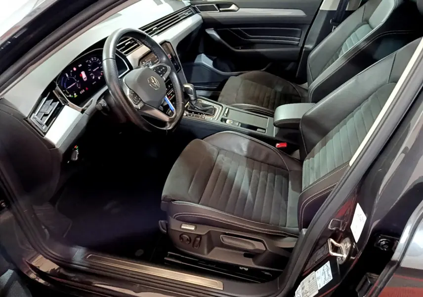 Vue intérieure côté conducteur de la Volkswagen Passat hybride rechargeable 2022, sièges noirs et tableau de bord digital.