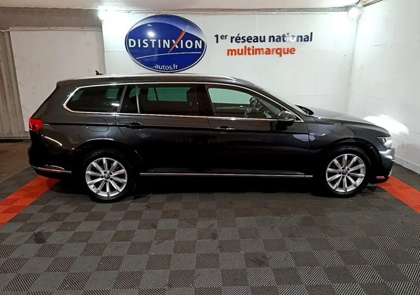 Profil droit d'une Volkswagen Passat SW GTE hybride rechargeable gris foncé dans un garage avec logo Distinxion en arrière-plan.