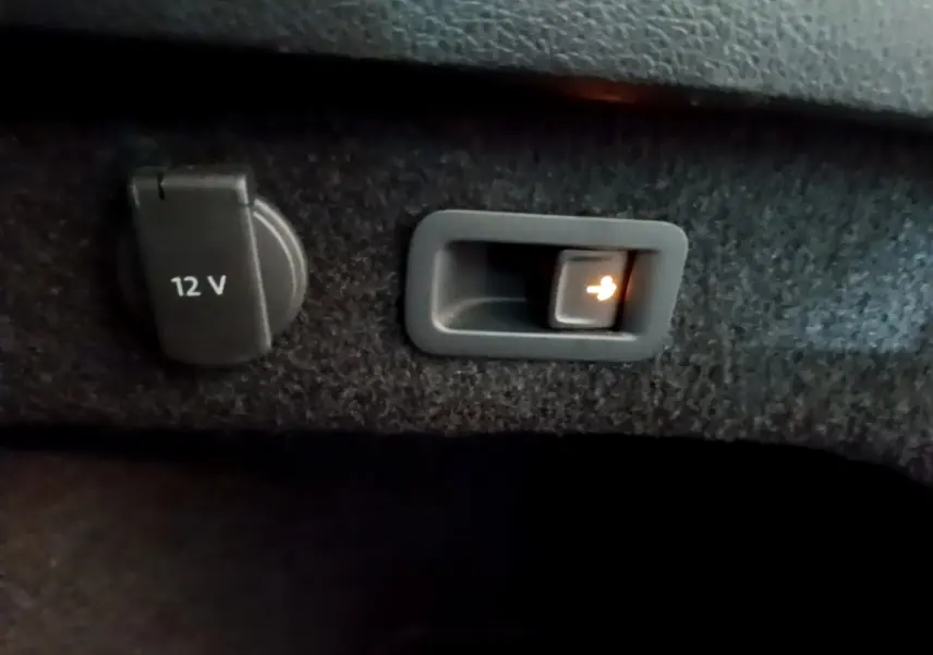 Prise 12V et bouton d'ouverture électrique du hayon dans le coffre de la Volkswagen Passat GTE hybride rechargeable gris foncé.