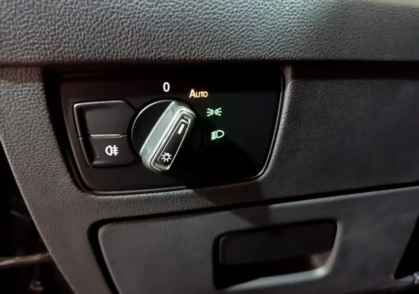 Gros plan sur le bouton de commande des phares avec réglage automatique dans l'habitacle noir de la Volkswagen Passat hybride.