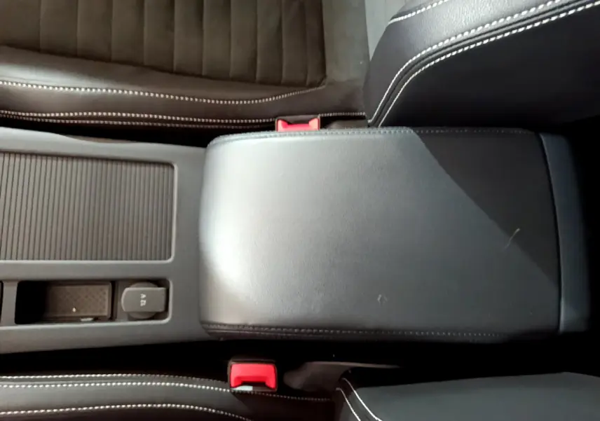 Gros plan sur la console centrale noire avec accoudoir cuir et sièges en tissu gris foncé de la Volkswagen Passat hybride rechargeable.