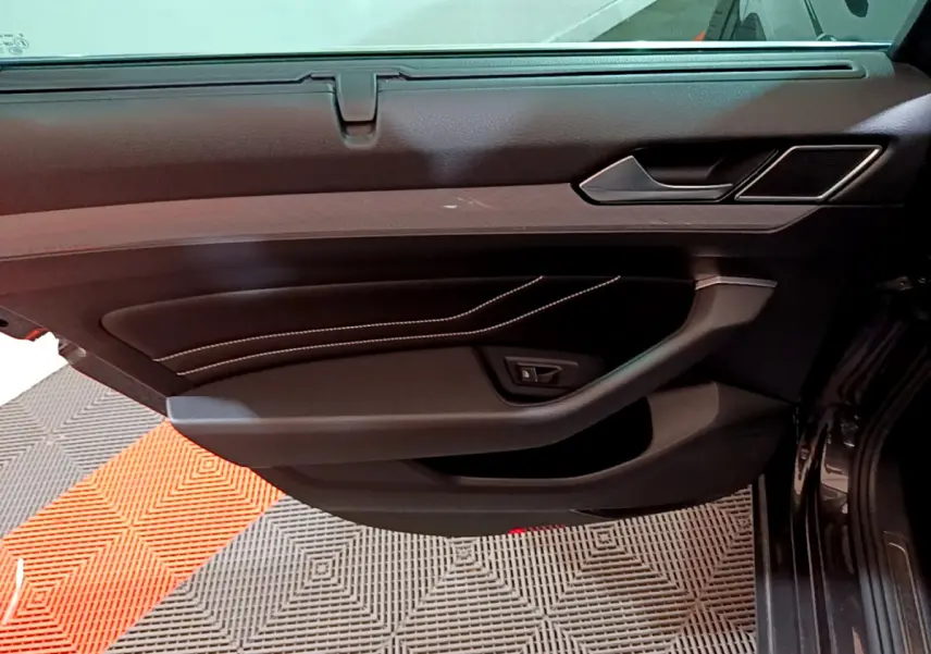 Porte intérieure côté gauche de la Volkswagen Passat GTE 2022 gris foncé, avec surpiqûres blanches et poignée intégrée.