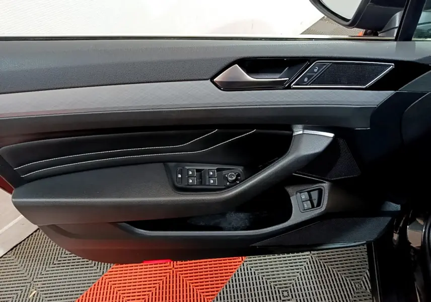 Panneau de porte côté conducteur noir avec commandes électriques et surpiqûres blanches dans une Volkswagen Passat GTE 2022.