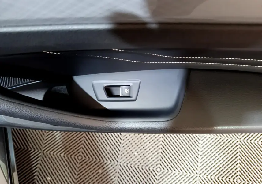 Détail de la poignée intérieure de porte côté gauche en plastique noir avec surpiqûres blanches sur la garniture, Volkswagen Passat GTE 2022.
