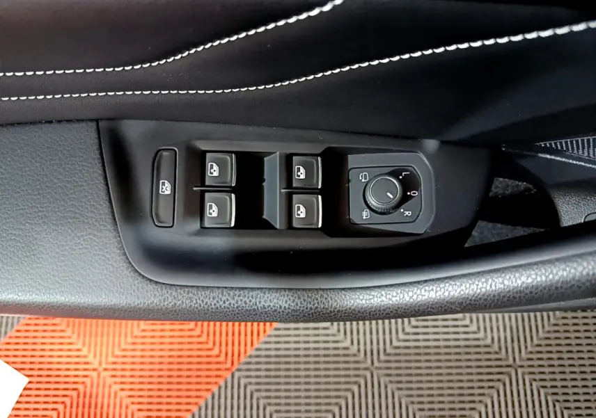 Gros plan sur les commandes de lève-vitres et réglage des rétroviseurs côté conducteur d'une Volkswagen Passat gris foncé 2022.