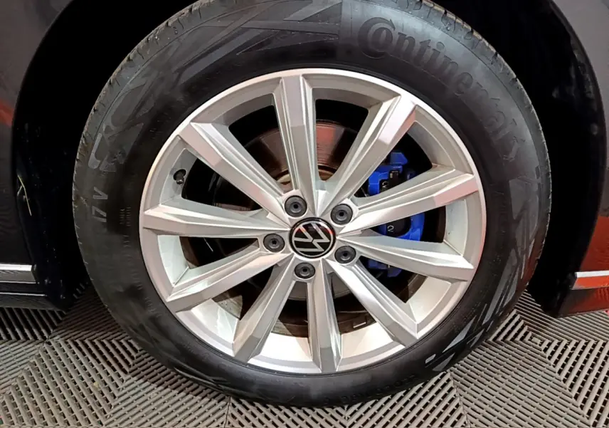 Gros plan sur la roue avant droite d'une Volkswagen Passat gris foncé, avec étrier de frein bleu visible.