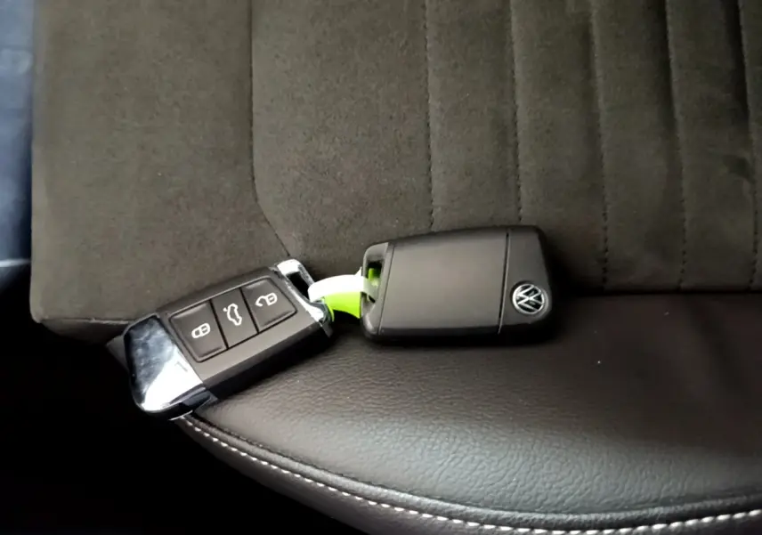 Clé noire Volkswagen posée sur un siège avant en tissu gris foncé et cuir noir avec surpiqûres blanches.