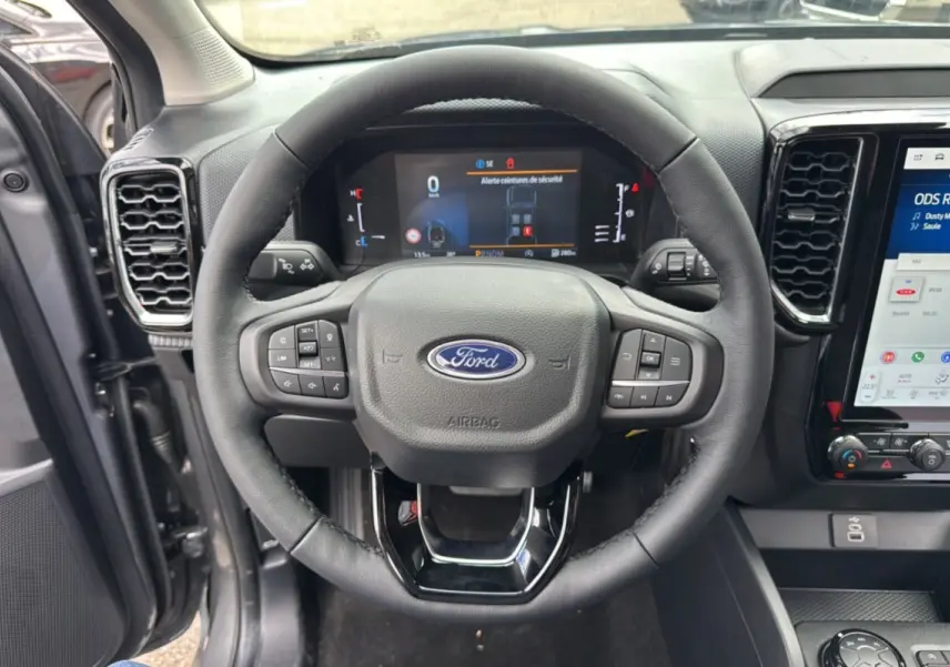 Vue intérieure centrée sur le volant du Ford Ranger 2025 gris carbone, avec tableau de bord numérique et écran tactile visible.