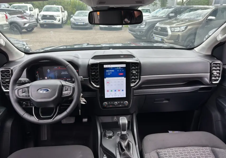 Vue intérieure du Ford Ranger 2025 gris carbone, mettant en valeur le tableau de bord moderne avec écran tactile vertical et volant multifonction.
