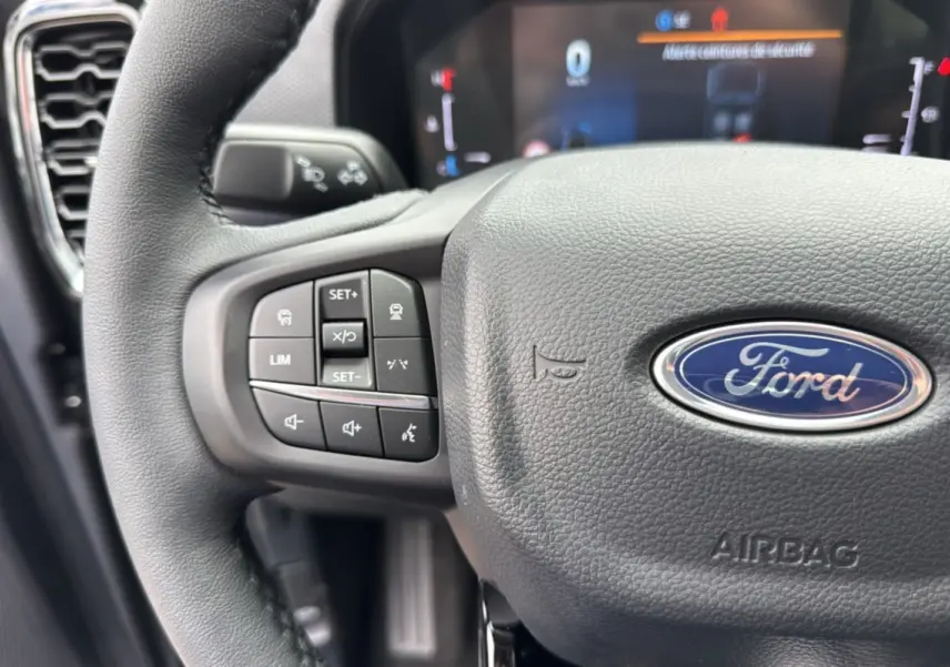 Gros plan sur le volant du Ford Ranger gris carbone 2025 avec commandes intégrées et tableau de bord numérique flou en arrière-plan