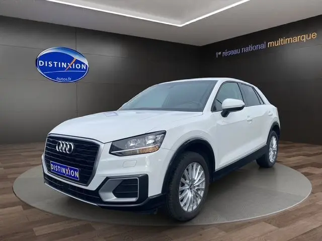 Audi Q2 blanc en 3/4 avant droit, mettant en valeur sa calandre noire et ses jantes alliage sur fond intérieur showroom.