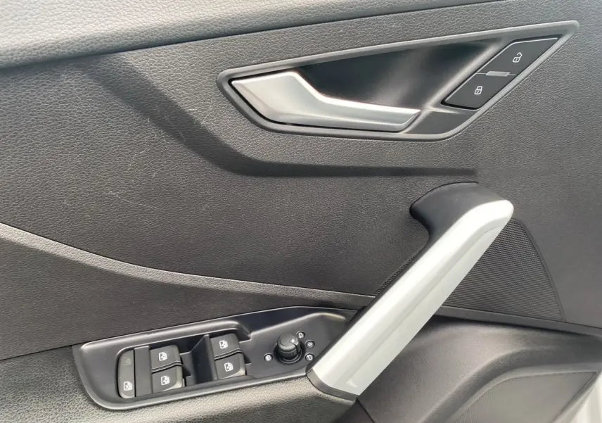 Poignée intérieure côté gauche de porte noire avec commandes de vitres et verrouillage d'une Audi Q2 blanche 2019.