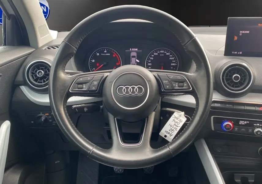 Vue rapprochée du volant noir d'un Audi Q2 30 TDI 2019 avec tableau de bord et écran central affichant la température.
