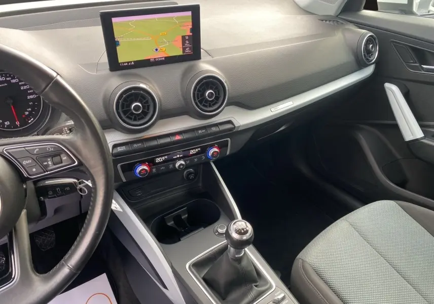 Vue intérieure côté conducteur de l'Audi Q2 blanc 2019, mettant en valeur la console centrale avec levier de vitesses manuel et écran GPS.