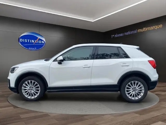 Profil droit d'un Audi Q2 blanc 2019 avec jantes alliage et toit contrasté noir dans un showroom moderne.
