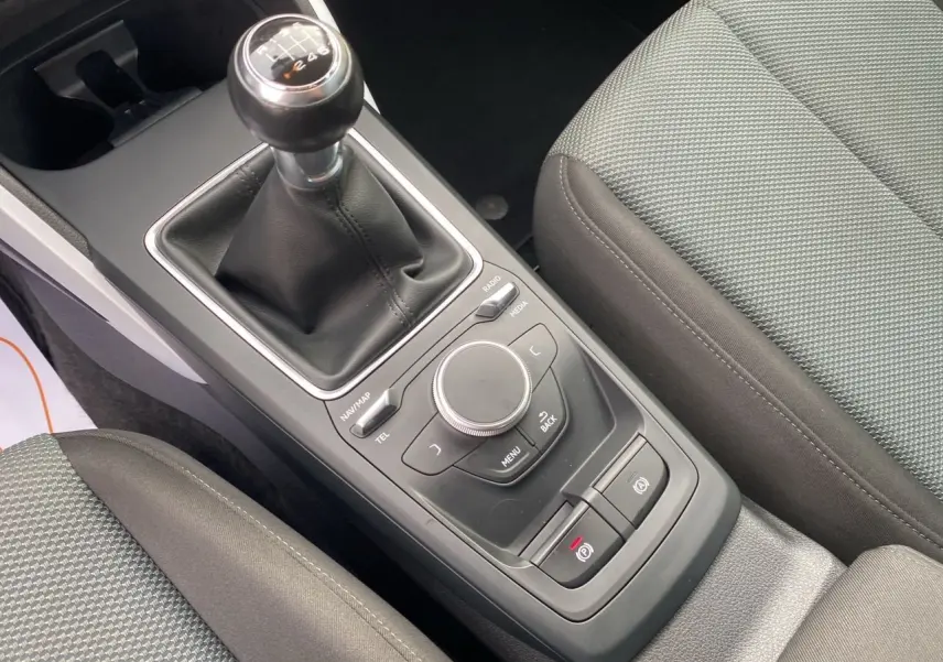 Vue rapprochée de la console centrale noire avec levier de vitesses manuel et sièges tissu gris de l'Audi Q2 blanc.