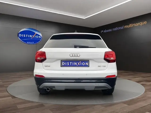 Vue arrière d'un Audi Q2 blanc 30 TDI 116 BVM6 de 2019 avec feux rouges et logo distinctif sur fond showroom.