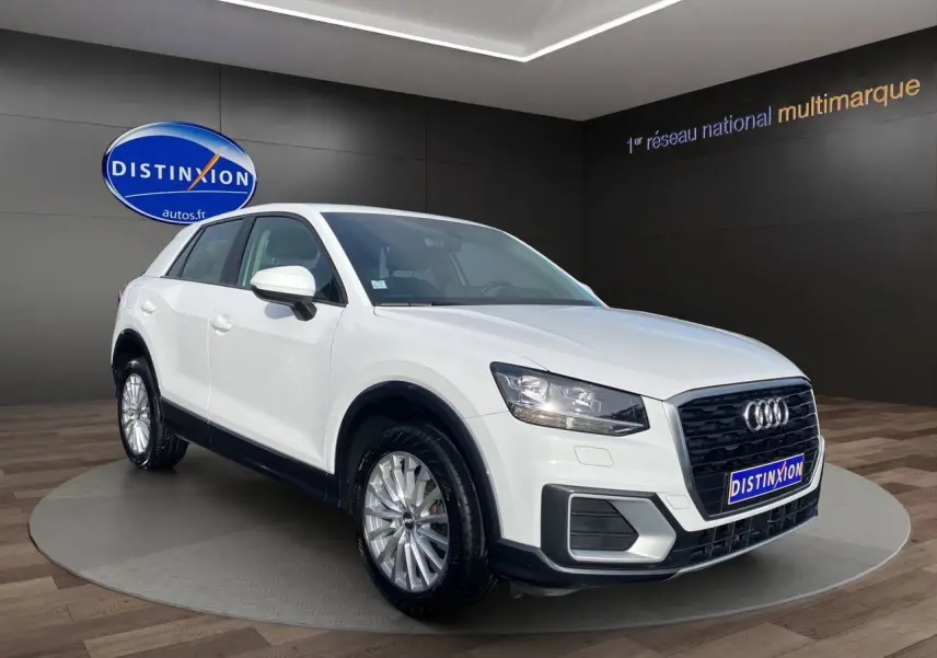 Audi Q2 blanc vue 3/4 avant droit, avec calandre noire et jantes alliage argentées, en showroom intérieur.