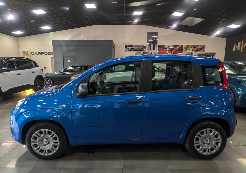 Vue de profil côté gauche d'une Fiat Panda 1.0 Hybrid 2025 en Bleu Italia, compacte et urbaine dans un showroom.