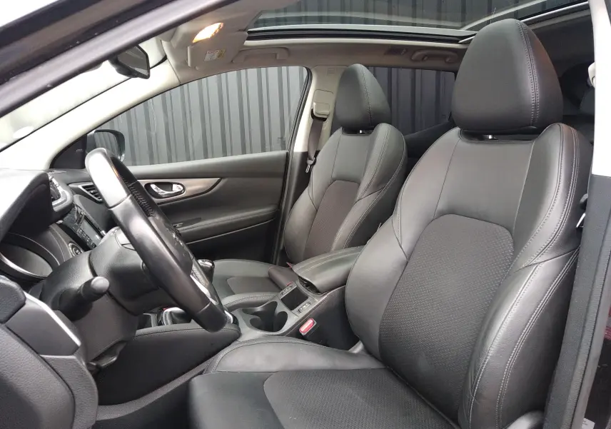 Vue intérieure côté conducteur du Nissan Qashqai 2019, sièges en cuir noir et toit ouvrant panoramique.