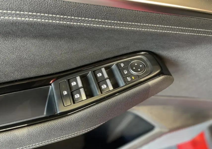 Gros plan sur les commandes de lève-vitres et rétroviseurs sur la porte côté conducteur d’une Renault Rafale rouge avec surpiqûres blanches.