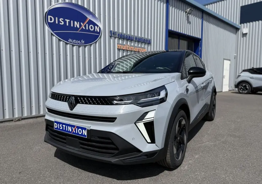 Renault Captur 2025 gris rafale avec toit noir, vu en 3/4 avant droit devant un bâtiment industriel.