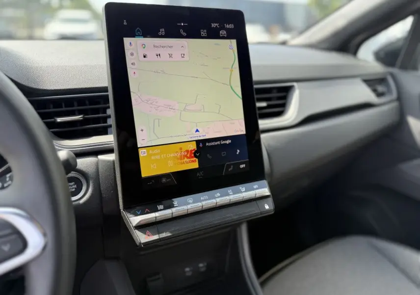 Vue intérieure du tableau de bord du Renault Captur 2025, écran tactile central affichant la navigation et commandes climatisation.