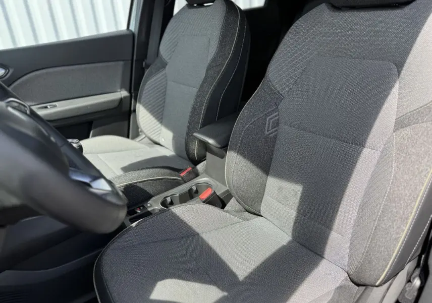 Vue intérieure rapprochée des sièges avant gris du Renault Captur 2025, mettant en valeur les textures et accoudoir central.