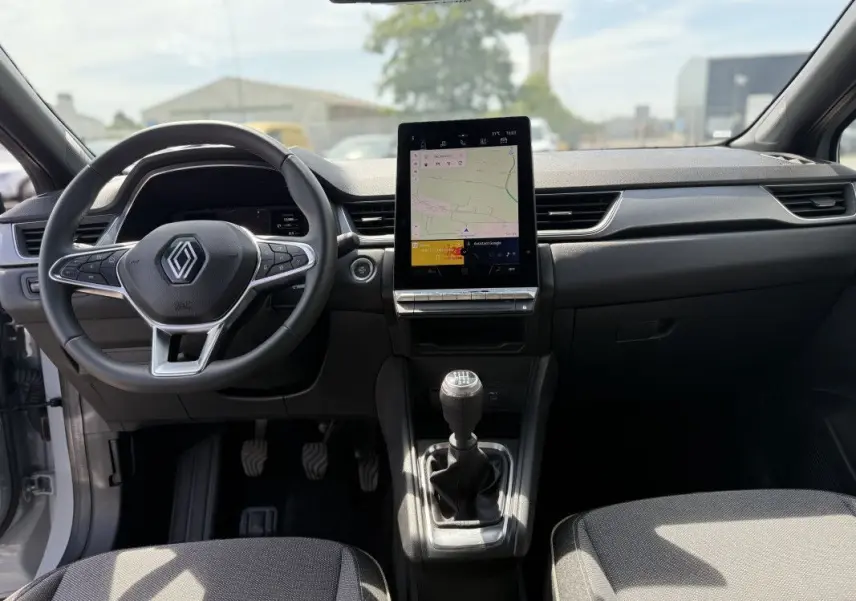 Vue intérieure avant du Renault Captur 2025, tableau de bord noir avec écran tactile vertical et levier de vitesse manuel.