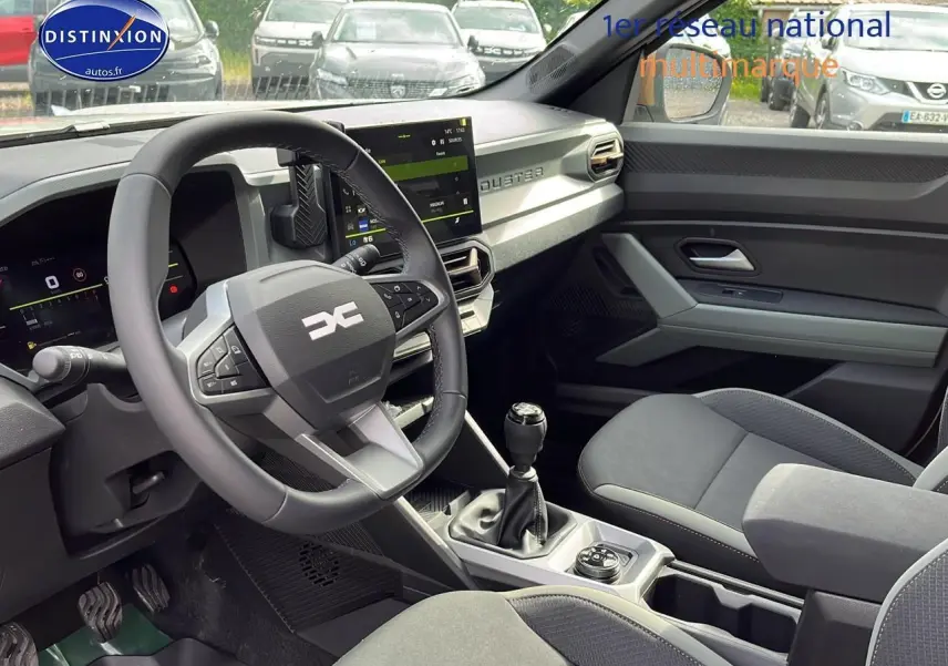Intérieur avant du Dacia Duster 2025 avec volant multifonction, écran tactile et sellerie grise moderne.