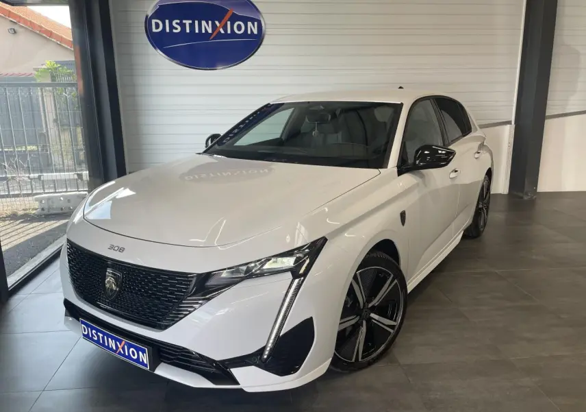 Peugeot 308 blanche vue 3/4 avant droit, avec calandre noire brillante et jantes alliage 18 pouces distinctives.