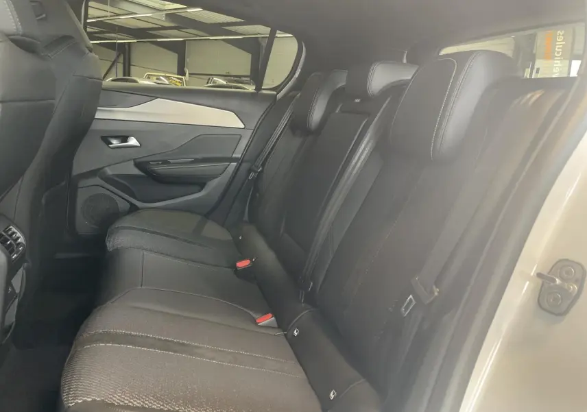 Vue intérieure côté droit sur la banquette arrière noire de la Peugeot 308 blanche avec surpiqûres et ceintures visibles.