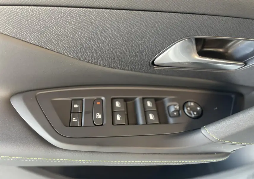 Gros plan sur la commande des vitres côté gauche d'une Peugeot 308 blanche, avec surpiqûres vertes sur la garniture.