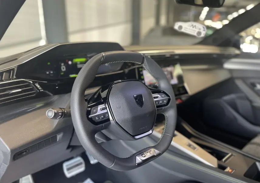 Vue intérieure du volant cuir Peugeot 308 GT 2025 avec combiné numérique et finitions noires et aluminium.