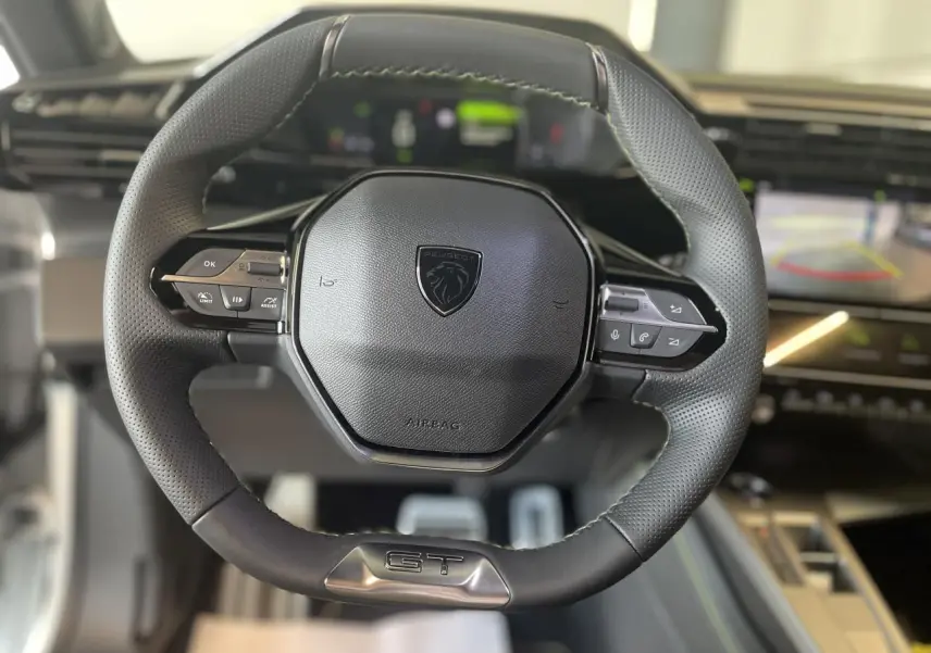 Volant cuir Peugeot 308 GT vu de face avec logo lion et commandes intégrées, intérieur moderne en arrière-plan flou.