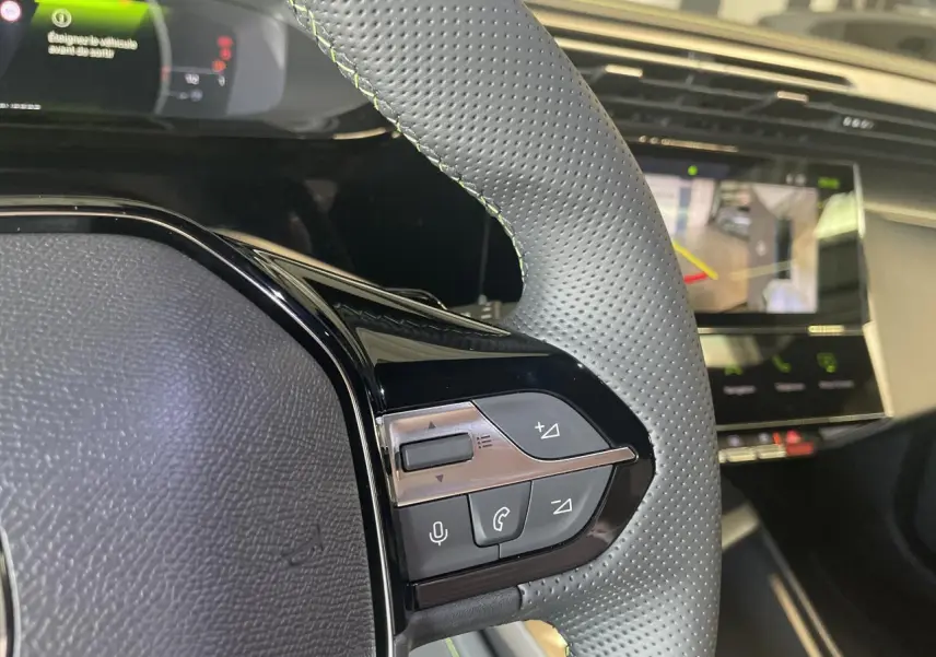 Gros plan sur le volant cuir perforé gris avec surpiqûres vertes et commandes multifonctions d'une Peugeot 308 blanche.