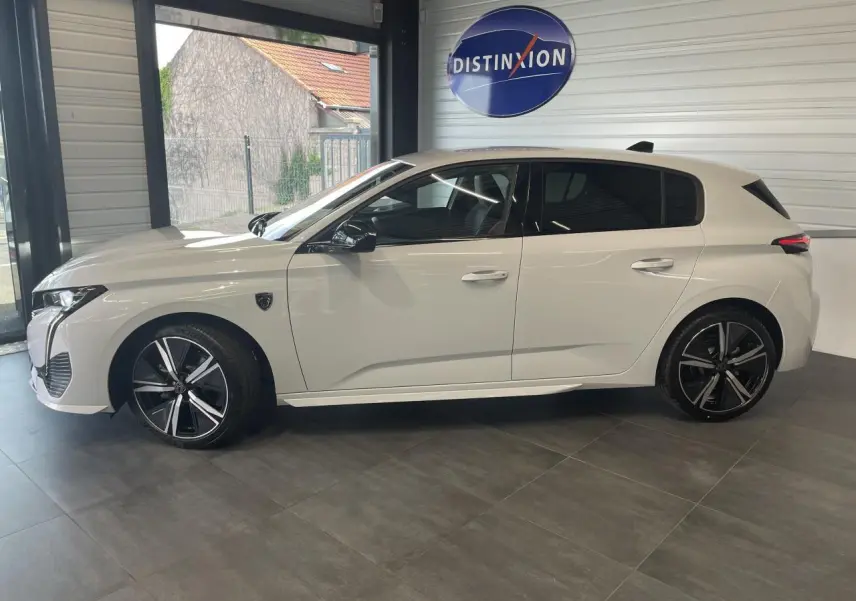 Peugeot 308 blanche vue de profil côté gauche, avec jantes alliage noires et vitres surteintées en intérieur showroom.