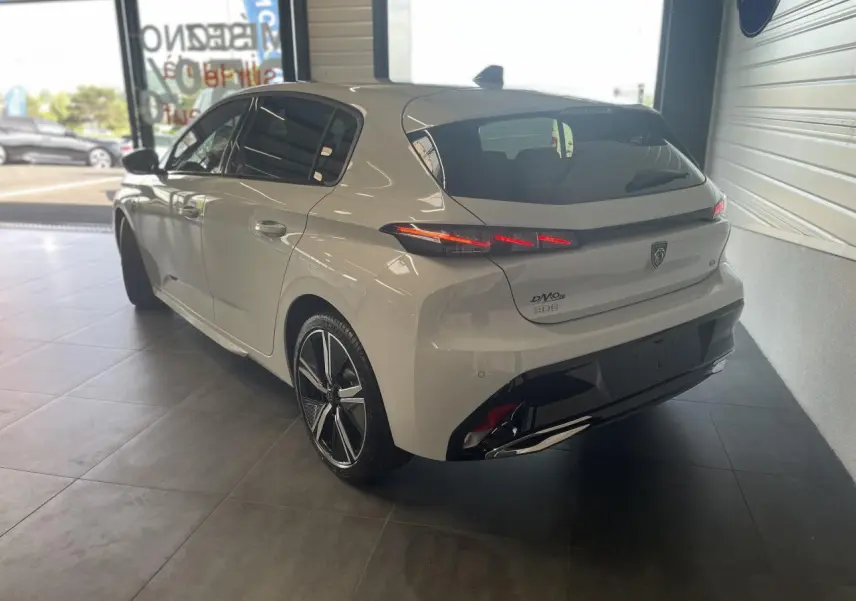 Peugeot 308 blanche vue 3/4 arrière droit en intérieur, avec feux arrière LED et jantes alliage noires.