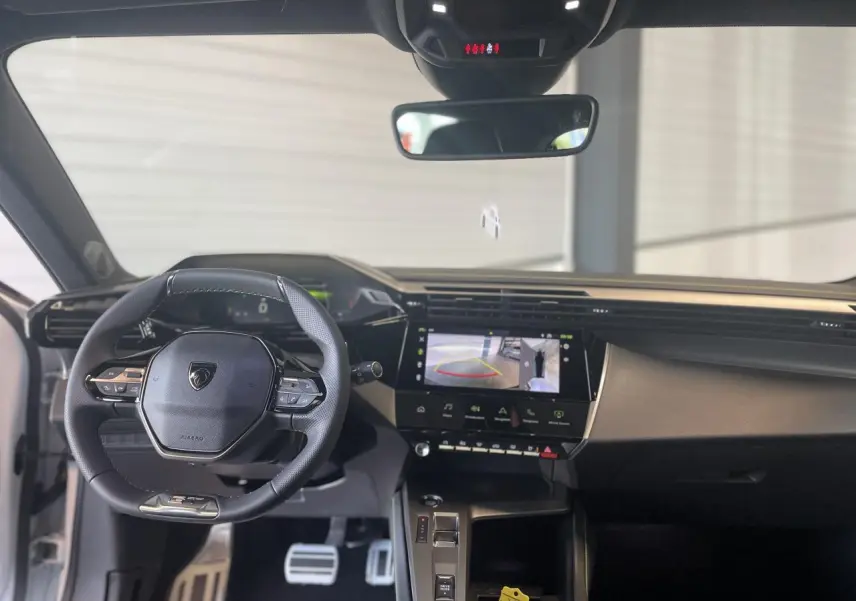 Vue intérieure avant de la Peugeot 308 2025 avec volant cuir, écran tactile et tableau de bord numérique.