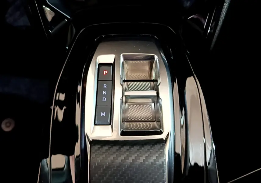 Gros plan sur la console centrale noire brillante avec sélecteur de boîte auto et commandes en finition carbone.