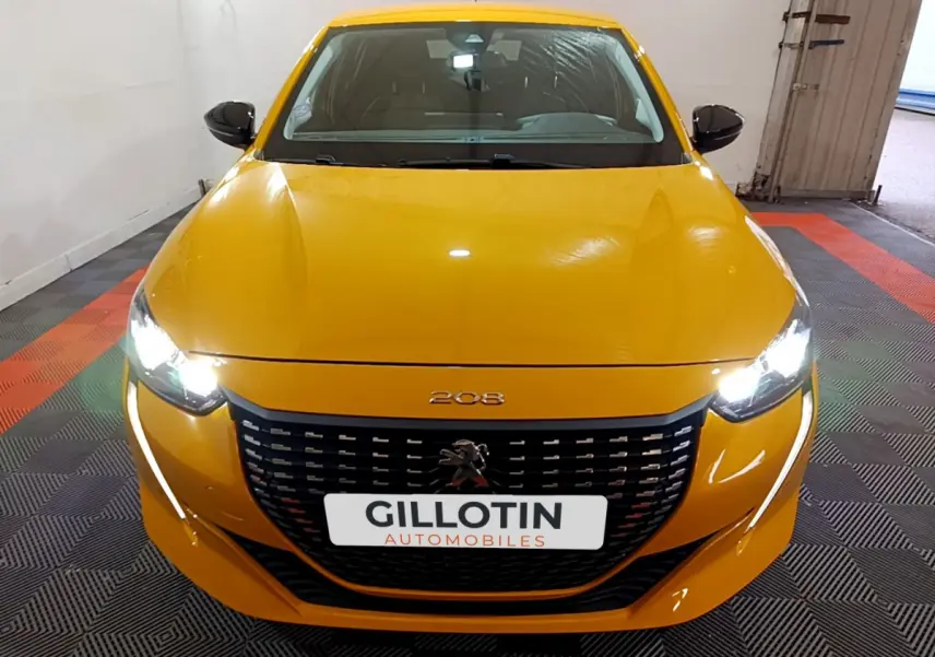 Peugeot 208 jaune vue de face avec phares allumés et calandre noire distinctive dans un garage.