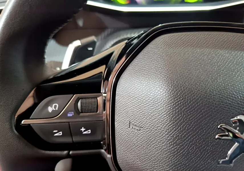 Gros plan sur le volant cuir noir de la Peugeot 208 jaune, avec commandes audio et logo lion visible.